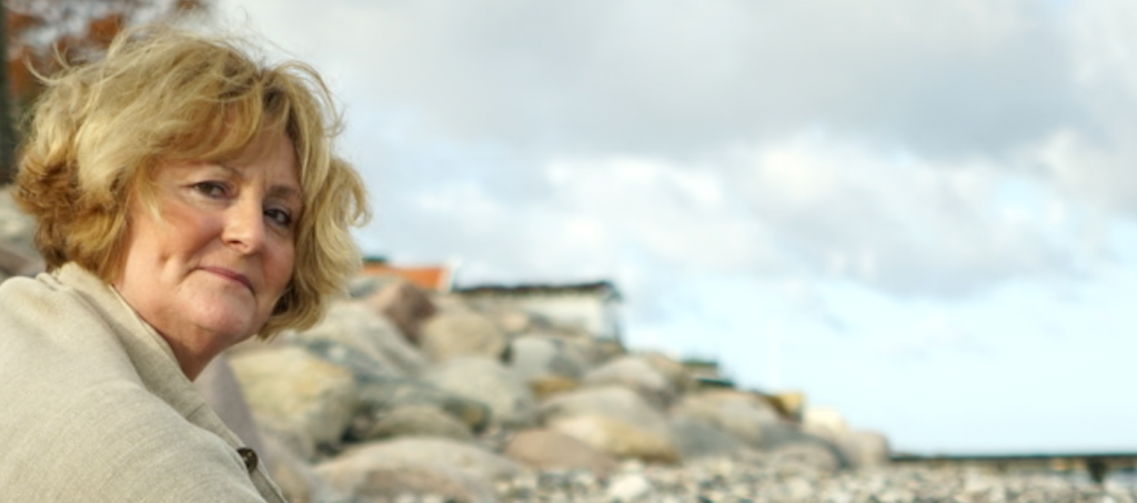 Susanne sidder ved stranden i Ålsgårde og kigger ind mod kameraet