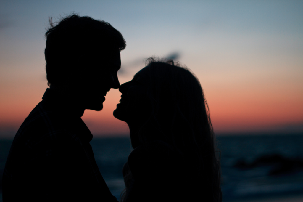 En ung mand og en ung kvinde ses i silhouet med en solnedgang bag dem. De smiler og er tætte på hinanden. Deres nærhed skyldes måske en god samtale med en sexolog.